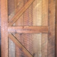 A rustic wooden barn door with vertical planks and a diagonal brace forming a Z pattern. The door displays a natural wood grain and warm brown tones, giving it a vintage, handcrafted appearance.