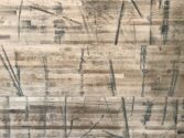 A wooden surface with a mix of light and dark wood tones, featuring marks and scratches in various directions, creating an abstract, textured pattern.