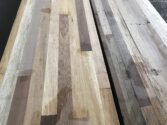 Close-up of a wooden tabletop featuring a patchwork of different wood types, showcasing a variety of textures and natural colors including light and dark browns. The surface is elongated and has a smooth finish.