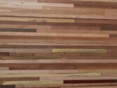 A wooden wall with horizontal strips of various shades and textures, ranging from light tan to dark brown. The different wood grains and colors create a natural, rustic pattern.